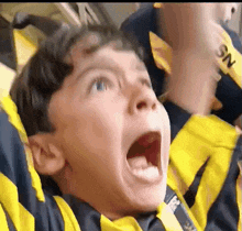 a young boy wearing a yellow and black striped shirt is screaming with his mouth open