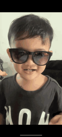 a young boy wearing sunglasses and a black shirt with the letter u on it