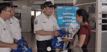 a man giving a bag to a woman in front of a sign that says " selamat hari pelangg nasional 2019 "