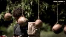 a man is standing in front of a wooden block with balls hanging from it and a rope around his head .