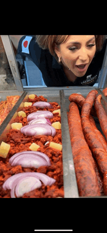 a woman is looking through a window at a display of meats and onions