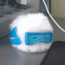 a white furry object with a blue face sits on a table