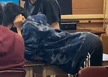 a man in a blue camo sweatshirt is laying on a desk in a classroom .