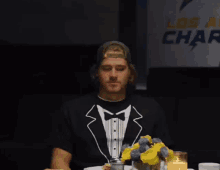 a man wearing a tuxedo shirt sits at a table in front of a sign that says los angeles chargers