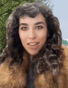 a woman with curly hair wearing a fur coat is smiling