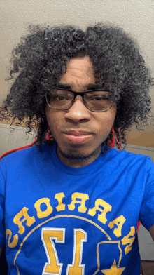 a man with curly hair wearing glasses and a blue shirt that says ' aoiaaa ' on it