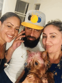 a man with a beard wearing a hat that says 21st century is surrounded by two women and a small dog