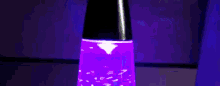 a purple lava lamp is sitting on a table with a purple wall in the background .