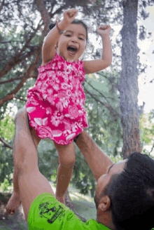 a little girl in a pink dress is being held up in the air by a man wearing a green shirt with a skull on it