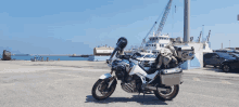 a blue and white motorcycle is parked in a parking lot with a boat in the background