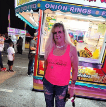 a woman stands in front of a onion rings stand at a carnival