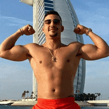 a shirtless man in red shorts is flexing his muscles in front of a large building .