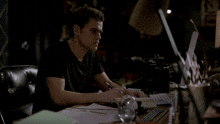 a man in a black shirt sits at a desk with a laptop