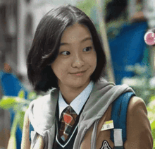 a young girl in a school uniform and tie is smiling and looking at the camera .