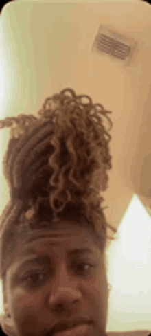 a woman with dreadlocks in a bun is taking a selfie with her phone .