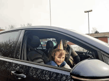 a little boy wearing a birthday hat is sitting in the back seat of a car