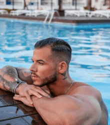 a shirtless man with a tattoo on his neck leans on the edge of a swimming pool