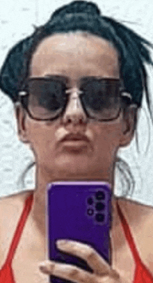 a woman wearing sunglasses is taking a selfie with a purple phone .