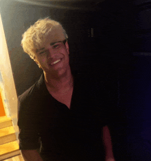 a young man with blonde hair and a black shirt smiles for the camera