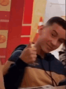 a young man is giving a thumbs up sign while sitting at a table in a restaurant .