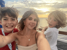 a woman takes a selfie with two children on a boat at sunset