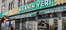 a man stands in front of a restaurant with a green sign that says ' ananin yeri '