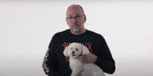 a man holding a small white dog wearing a black shirt that says txxx