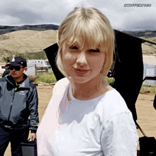 a woman in a white t-shirt is standing in a field with a man in a black hat behind her