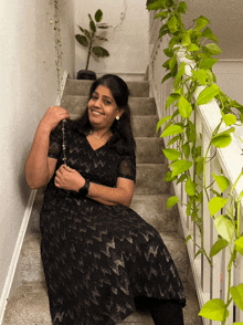 a woman in a black dress is sitting on a set of stairs next to a plant