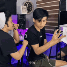 two young men are sitting in front of a clock and a sign that says " you 're very pretty person "