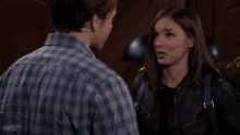 a man in a plaid shirt and a woman in a leather jacket looking at each other