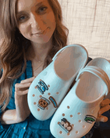 a woman holds a pair of crocs with stickers on them including pretzel gang