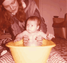 a woman is holding a baby in a yellow tub