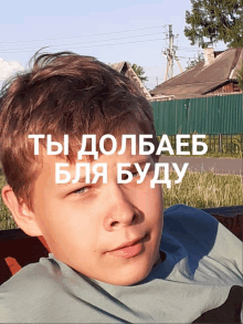 a boy is laying on a bench in front of a sign that says " ты долбаеb "