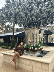 a woman sits in front of a fountain in front of a restaurant that says the gardens