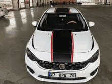 the front of a white car with black and red stripes on the hood is parked in a parking lot .