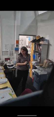 a woman in a leopard print shirt is standing in a cluttered room