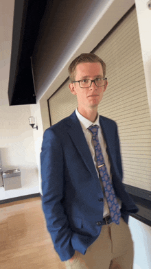 a man in a blue suit and tie stands in front of a window