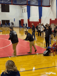 a group of wrestlers on a gym floor with a man wearing a black shirt with the letter t on it