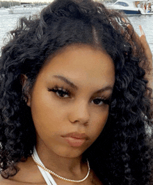 a woman with curly hair and a pearl necklace looks at the camera