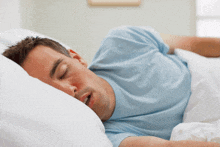 a man in a blue shirt is sleeping in a bed with his eyes closed