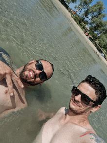 two shirtless men wearing sunglasses are standing in the water