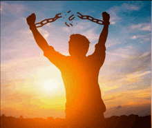 a silhouette of a man holding broken chains in front of a sunset