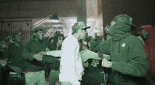 a group of people are standing around a man in a white shirt and a green hoodie