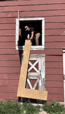 a man is holding a piece of wood in front of a red barn