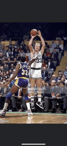 a basketball player is jumping in the air to throw the ball while another player watches .