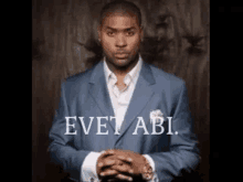 a man in a suit is standing with his hands folded in front of a sign that says evet abi .