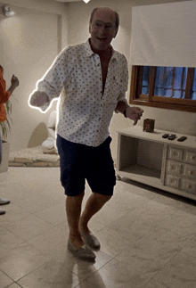 a man in a polo shirt and shorts is dancing in a room