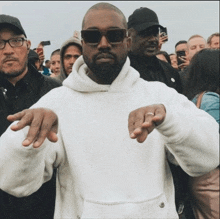 a man wearing a white hoodie and sunglasses stands in a crowd