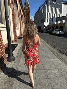 a woman in a red dress is walking down a cobblestone street in front of a building that says sd quisque